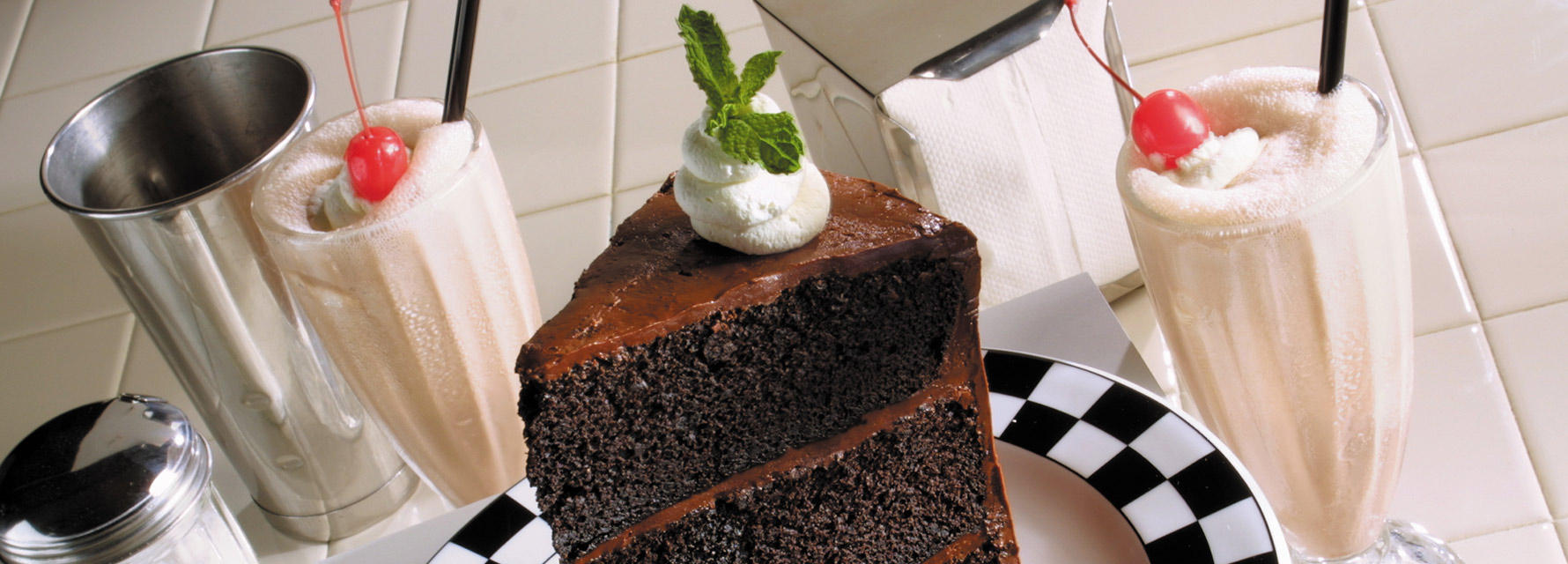 Slice of chocolate cake plated with two vanilla milkshakes.