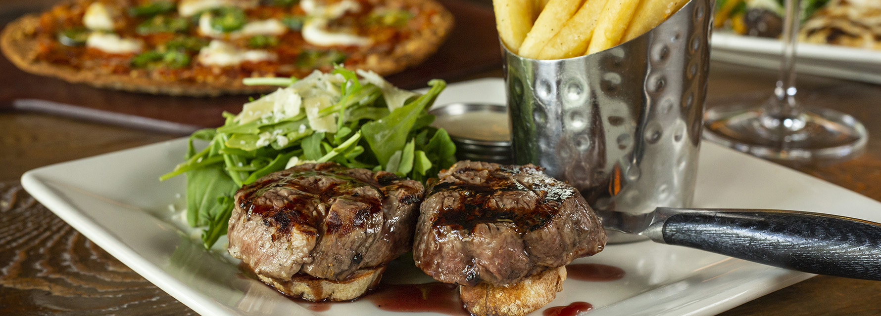 Twin filets with fries and flatbread pizza in background